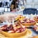 A hand reaching for a piece of grilled calamari on a table with a glass of wine and several plates of appetizers